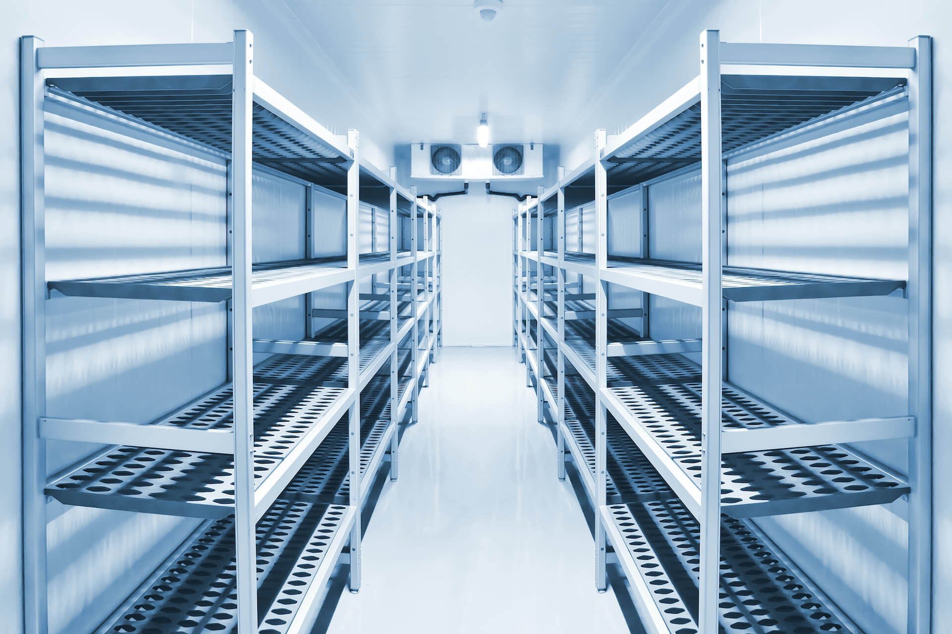 Aisle of empty stainless steel shelving units in a walk-in refrigerated storage room.