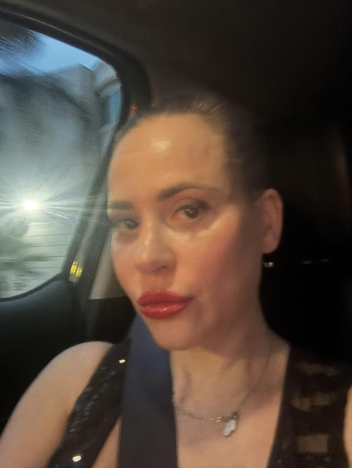 Screenshot 2026-09-27 at 22635 PM Close-up of a woman in a car wearing a seatbelt, with red lipstick and a dark top.